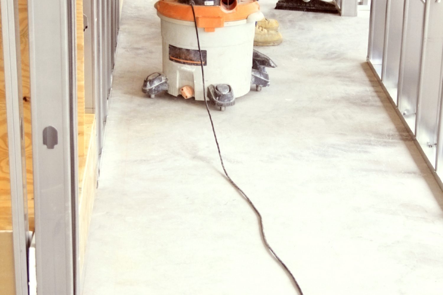 A construction worker vacuums the cement floor with a wet/dry vac.